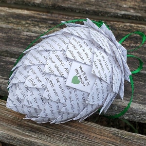 Puede incluir: Un corazón de papel blanco doblado en forma de piña, con una cinta verde. El corazón tiene un pequeño corazón verde en él con el texto "You'll be in my heart".