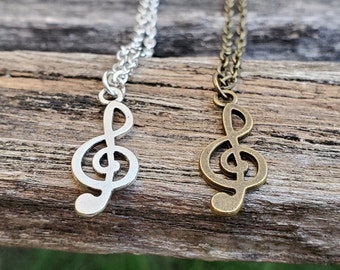 Puede incluir: Dos collares de plata y oro con colgantes de clave de sol. Los collares están sobre una superficie de madera.