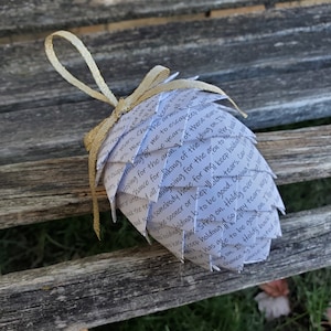 Pode incluir: Um enfeite de papel branco em forma de pinha com uma fita dourada. O enfeite &eacute; coberto com texto escrito &agrave; m&atilde;o, incluindo as palavras "escape", "hoping for", "chance for", "keep holding", "to be good", "holding on", "my tears", "every time", "keep tears", "good on", "choice", "holding", "so good".