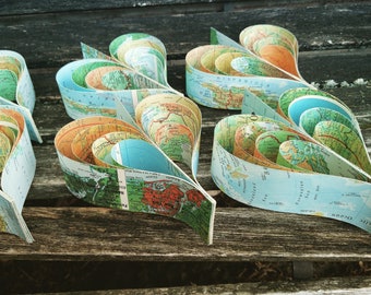 May include: A collection of five heart-shaped paper crafts made from vintage maps. Each heart is layered with different colored maps, creating a unique and colorful design.