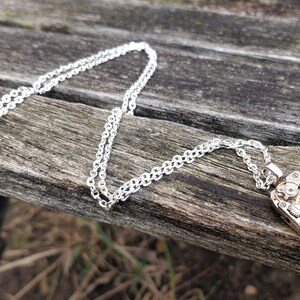 May include: A silver chain necklace with a silver pendant featuring a detailed clockwork design. The pendant is rectangular and has visible gears and other clock parts.