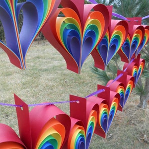May include: A rainbow paper heart garland with red, orange, yellow, green, blue, indigo, and violet paper hearts strung together with purple string.
