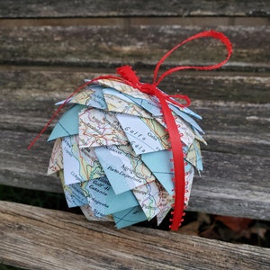 May include: A blue and white map globe ornament with a red ribbon. The globe is made of paper and has a textured surface. The ribbon is tied around the globe and has a red fringe.