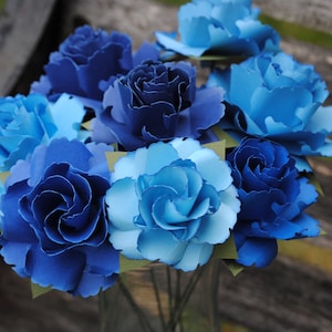 May include: A bouquet of blue and light blue paper flowers. The flowers are arranged in a vase and are made to look like roses.