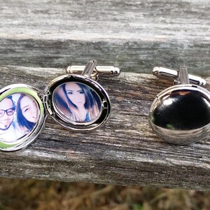 May include: A pair of silver cufflinks with a round locket design. One locket is open and shows a photo of a couple, while the other locket is closed.