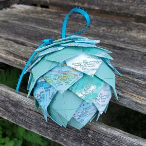 May include: A teal blue and white globe ornament made from a map of the Caribbean islands. The ornament is made of folded paper and has a teal blue ribbon attached.