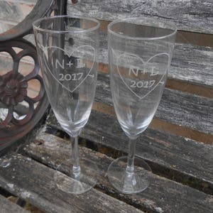 May include: Two clear glass champagne flutes with etched hearts and the text "N+L 2017".