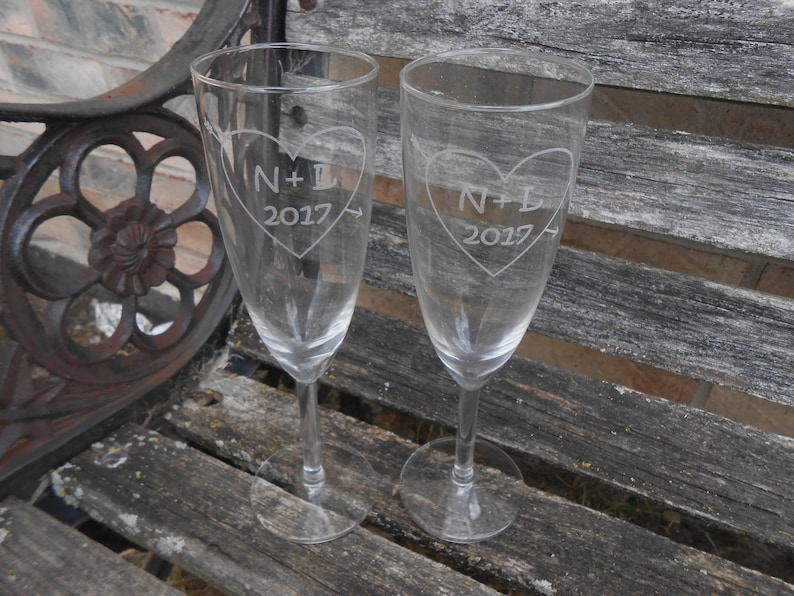 May include: Two clear glass champagne flutes with etched hearts and the text "N+L 2017".