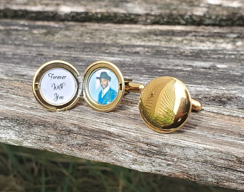 May include: Gold cufflinks with a round, hinged locket. The locket opens to reveal a black and white photo of a man wearing a hat and a blue patterned shirt. The inscription on the locket reads "Forever With You".