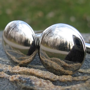 May include: A pair of silver cufflinks with a reflective surface. The cufflinks are round and have a smooth finish.