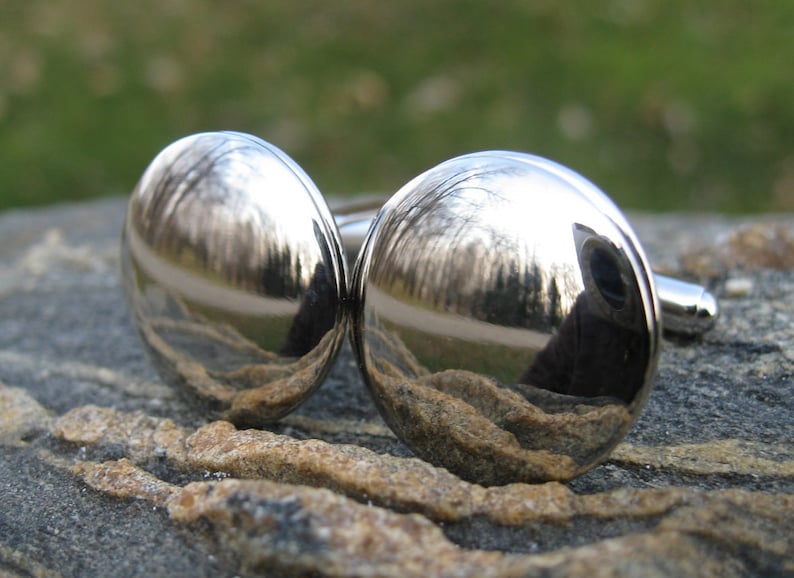 May include: A pair of silver cufflinks with a reflective surface. The cufflinks are round and have a smooth finish.