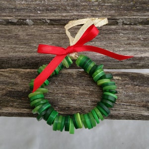 Puede incluir: Una corona de botones verdes con un lazo rojo y una cinta dorada.