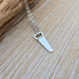 May include: A silver saw pendant necklace. The saw is a simple design with a pointed tip and a handle.