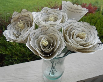 Puede incluir: Un ramo de cinco flores de papel hechas con las páginas de libros antiguos. Las flores son blancas y tienen un aspecto delicado y vintage. Cada flor tiene un pequeño grupo de cuentas blancas en el centro.