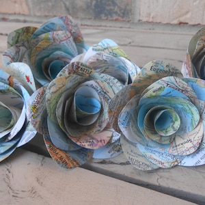 May include: A bouquet of paper roses made from vintage world maps. The roses are blue and white and feature city names like Seattle, New York, and Mombasa.