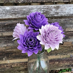May include: A bouquet of purple and white paper flowers. The flowers are made from pages of a book and have a delicate, romantic look.