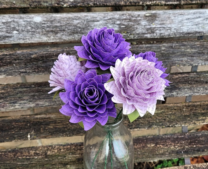 May include: A bouquet of purple and white paper flowers. The flowers are made from pages of a book and have a delicate, romantic look.