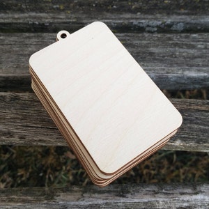 May include: A stack of unfinished, rectangular wooden tags with a hole at the top. The tags are light brown and have a smooth surface.