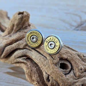 May include: A pair of gold and silver bullet earrings with the text "9mm Luger Blazer" and "9mm Luger" on them.