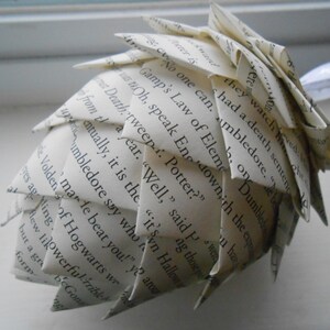 May include: A white paper pinecone ornament made from pages of a book. The text on the pages is visible and reads "No one can...Gamp's Law of Elements...Dumbledore...Potter?"