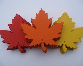 May include: A stack of orange, red, and yellow paper maple leaves. The leaves are cut out and have a hole in the center.