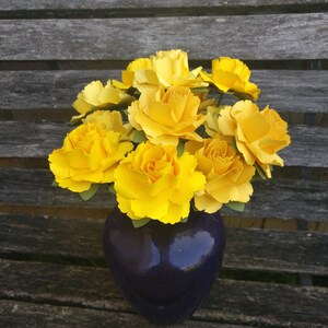 May include: A bouquet of yellow paper flowers in a dark purple vase. The vase is sitting on a wooden surface.