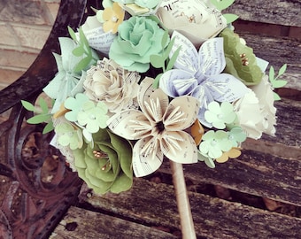 May include: A bouquet of paper flowers made from sheet music and green paper. The bouquet is tied together with a brown ribbon and has a light brown handle.