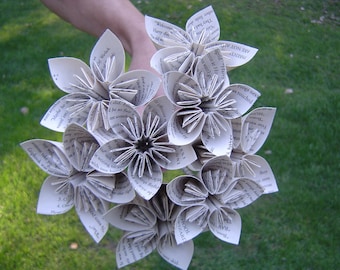 Puede incluir: Un ramo de flores de papel blanco hechas con las páginas de un libro. Las flores están dispuestas en forma circular y tienen un aspecto delicado y vintage. El texto en las páginas es visible, incluyendo las palabras "Harry Potter" y "El niño que sobrevivió".