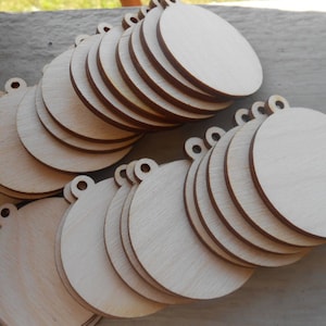 May include: A stack of unfinished wooden round ornaments with a hole at the top for hanging. The ornaments are all the same size and are made of light-colored wood.
