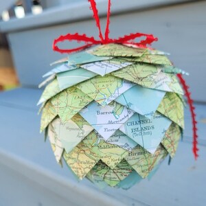May include: A Christmas ornament shaped like a pine cone made from folded maps of the United Kingdom. The ornament is decorated with a red ribbon.