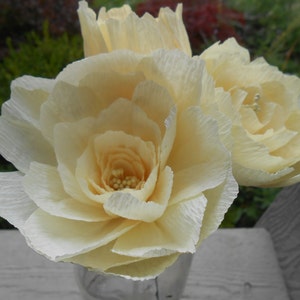 May include: Three cream-colored paper flowers in a glass vase. The flowers are made of crinkled paper and have a delicate, romantic look.