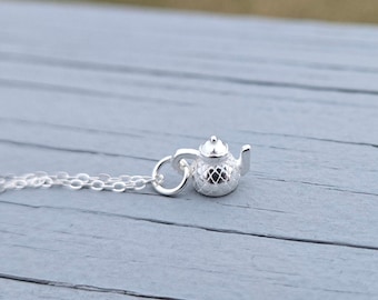 May include: A silver necklace with a small teapot charm. The teapot has a textured surface and a delicate design.