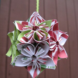 May include: A red, white, and green paper ornament with a candy cane pattern. The ornament is made of origami paper and is shaped like a flower.