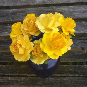 May include: A bouquet of yellow paper flowers in a blue vase. The flowers are arranged in a circular shape and have a realistic appearance.