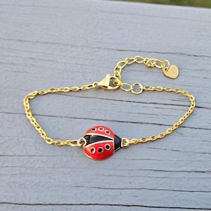 Peut inclure: Un bracelet en chaîne dorée avec un charme de coccinelle rouge et noire. Le charme a des points noirs sur les ailes et un contour doré.