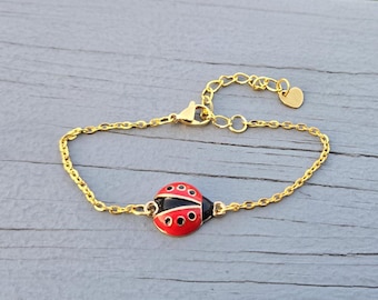 Puede incluir: Un brazalete de cadena dorada con un dije de mariquita roja y negra. El dije tiene puntos negros en las alas y un contorno dorado.