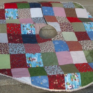 May include: A patchwork Christmas tree skirt with a white lace trim. The skirt is made of various fabrics in red, green, blue, and white, with a variety of patterns.