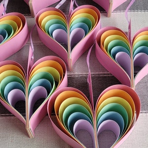 K&ouml;nnte beinhalten: Ein Satz Regenbogen-Papierherzen, jedes aus mehreren Schichten Papier in den Farben Rot, Orange, Gelb, Gr&uuml;n, Blau, Indigo und Violett. Die Herzen sind in einer Reihe angeordnet, wobei das gr&ouml;&szlig;te Herz oben und das kleinste Herz unten ist.
