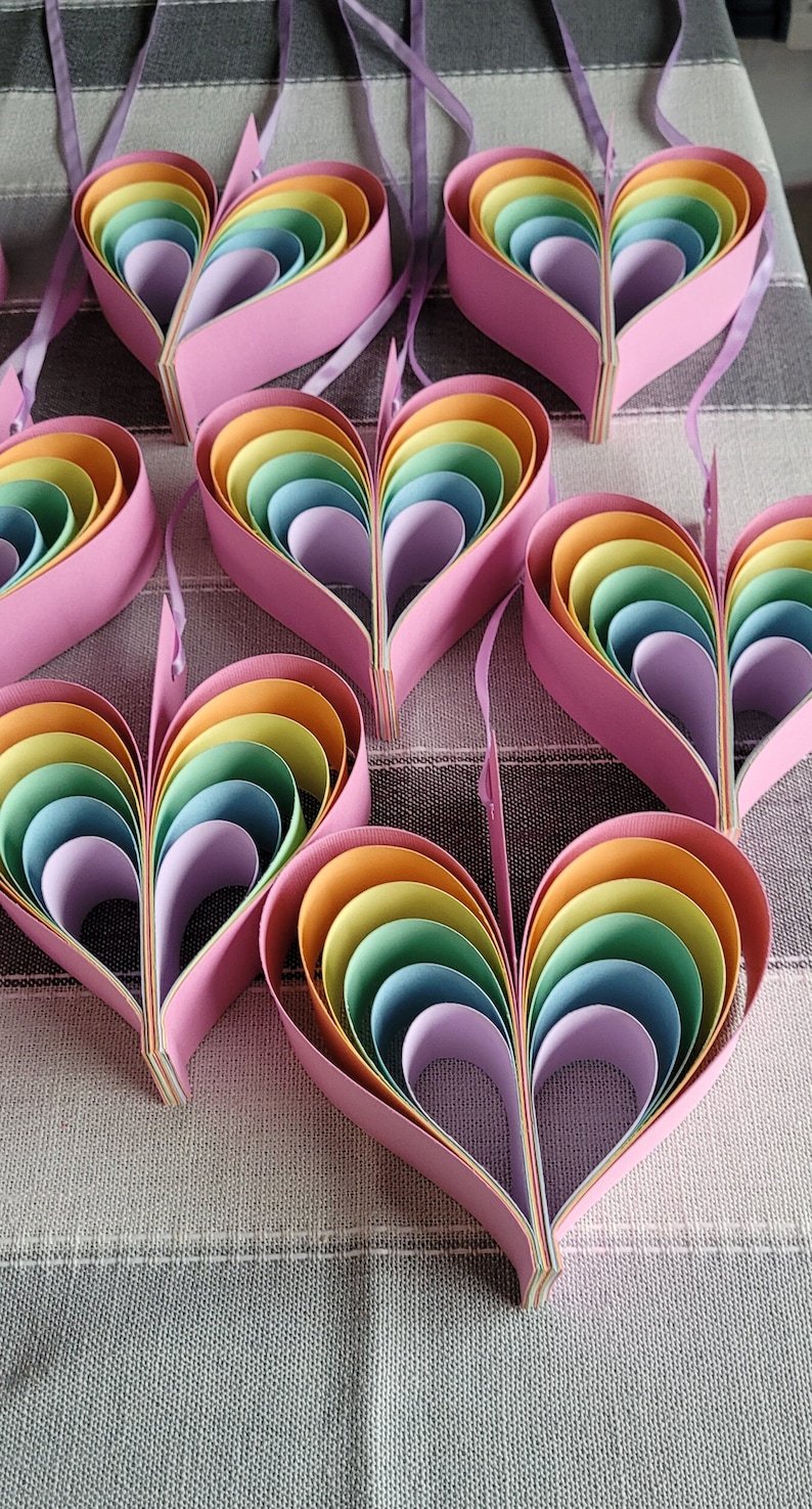 K&ouml;nnte beinhalten: Ein Satz Regenbogen-Papierherzen, jedes aus mehreren Schichten Papier in den Farben Rot, Orange, Gelb, Gr&uuml;n, Blau, Indigo und Violett. Die Herzen sind in einer Reihe angeordnet, wobei das gr&ouml;&szlig;te Herz oben und das kleinste Herz unten ist.