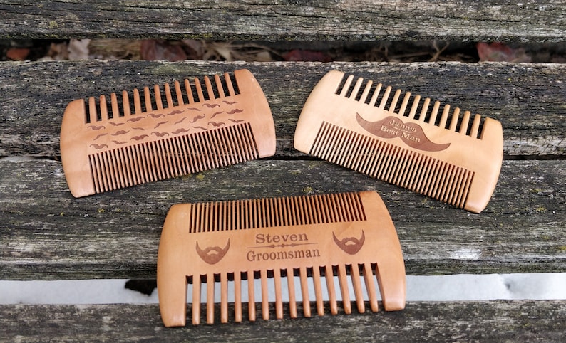 Peut inclure: Trois peignes en bois avec des motifs diff&eacute;rents. Le premier peigne a un motif de petites moustaches. Le deuxi&egrave;me peigne a le texte "James Best Man" et une moustache. Le troisi&egrave;me peigne a le texte "Steven Groomsman" et une barbe.