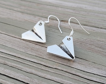 May include: A pair of silver earrings shaped like paper airplanes. The earrings have a simple design and are a great way to add a touch of whimsy to any outfit.