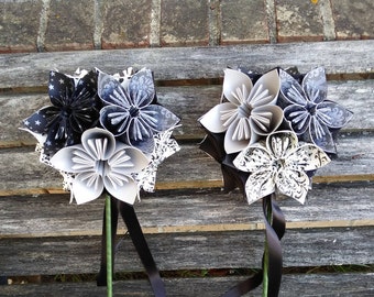 Puede incluir: Dos ramos de flores de origami en blanco y negro con tallos de cinta negra. Las flores están hechas de papel estampado y están dispuestas en forma circular.