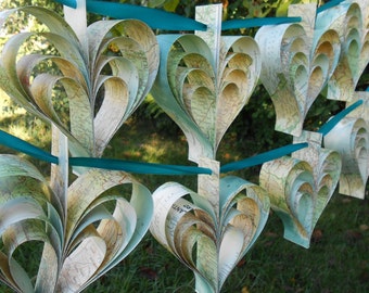 May include: A string of paper hearts made from maps, hanging from a teal ribbon. The hearts are folded in a layered pattern, creating a three-dimensional effect.