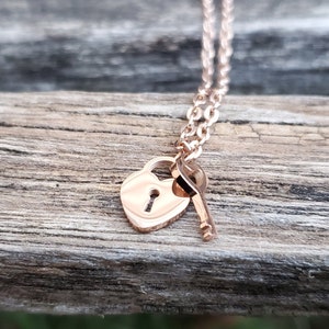 Op de afbeelding: Een ketting van roségoud met een hartvormig hangslot en een sleutelbedel.