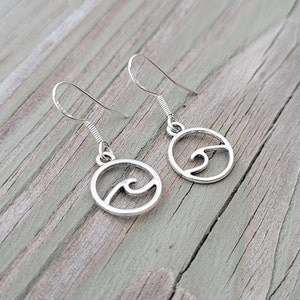 May include: Silver earrings with a wave design. The earrings are in the shape of a circle with a wave cut out of the center.