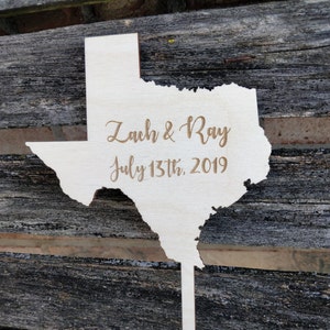 May include: A wooden cutout of the state of Texas with the text "Zach & Ray July 13th, 2019" engraved on it.