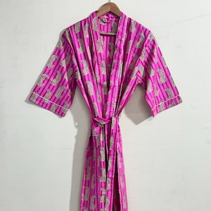 May include: A vibrant pink robe with vertical stripes and a repeating leopard print pattern. The robe has a matching belt and white trim along the edges. It is hanging on a wooden hanger.
