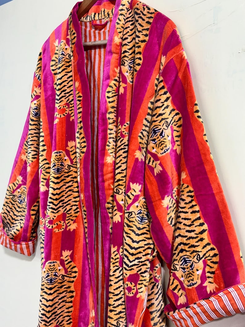 May include: A long-sleeved robe featuring a vibrant pattern of orange and black tigers set against vertical stripes of bright magenta and orange. The garment includes a solid magenta trim along the front opening and cuffs with a white and orange striped lining.
