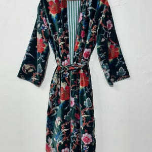 May include: A long-sleeved velvet robe in a deep forest green base color, featuring a vibrant floral pattern in shades of red, pink, blue, and white. The garment includes a matching tie belt at the waist and a white and green striped inner lining.