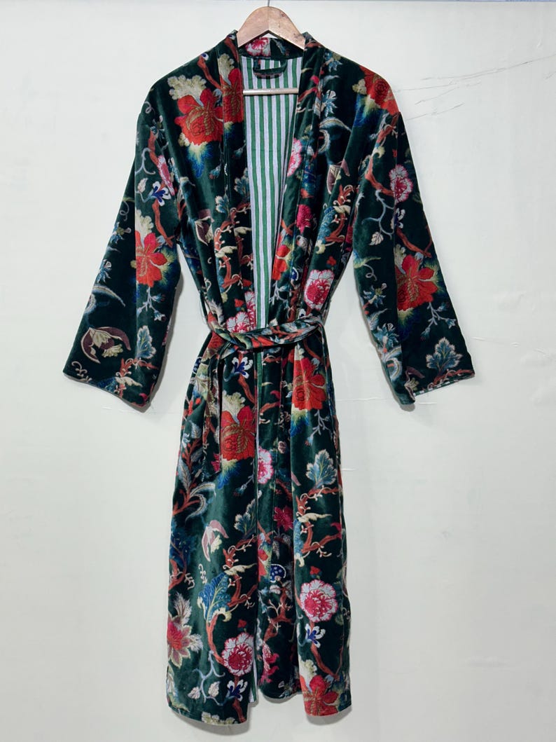 May include: A long-sleeved velvet robe in a deep forest green base color, featuring a vibrant floral pattern in shades of red, pink, blue, and white. The garment includes a matching tie belt at the waist and a white and green striped inner lining.